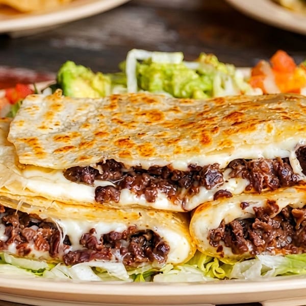 Cheesy beef quesadillas with lettuce, guacamole, pico de gallo, and sour cream on a plate.