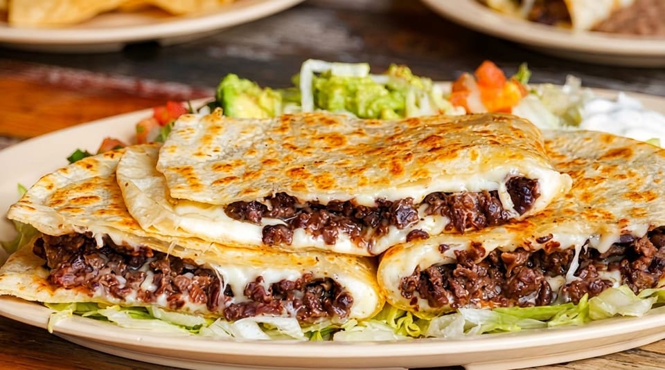 Cheesy beef quesadillas with lettuce, guacamole, pico de gallo, and sour cream on a plate.