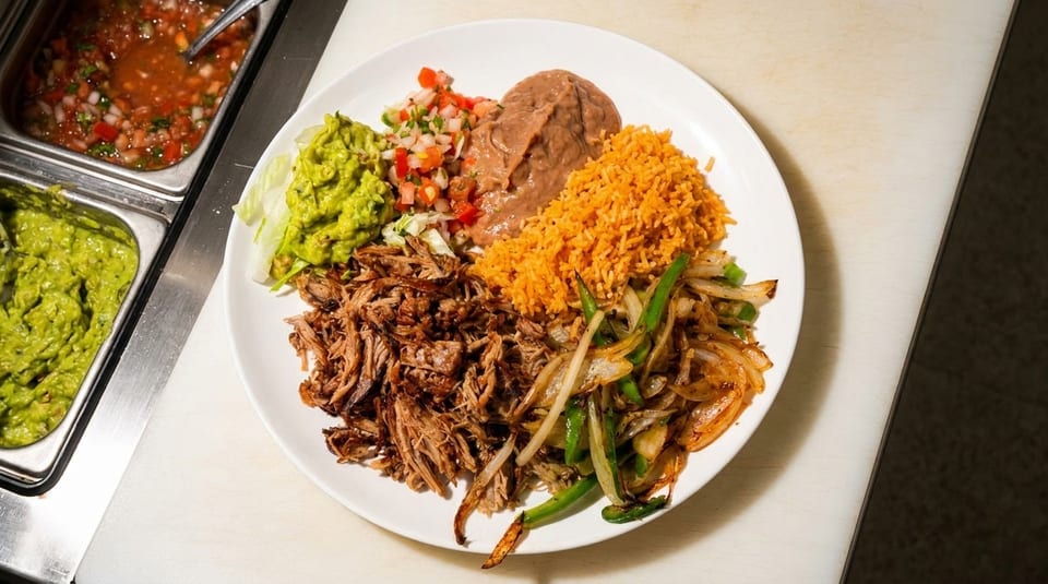 A plate of Mexican food with shredded pork, rice, beans, guacamole, pico de gallo, and fajita vegetables.